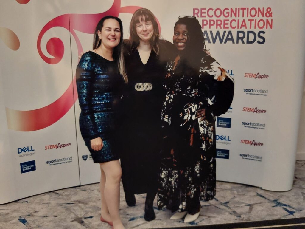 Three women standing in front of a wall banner that reads SAMEE Awards.